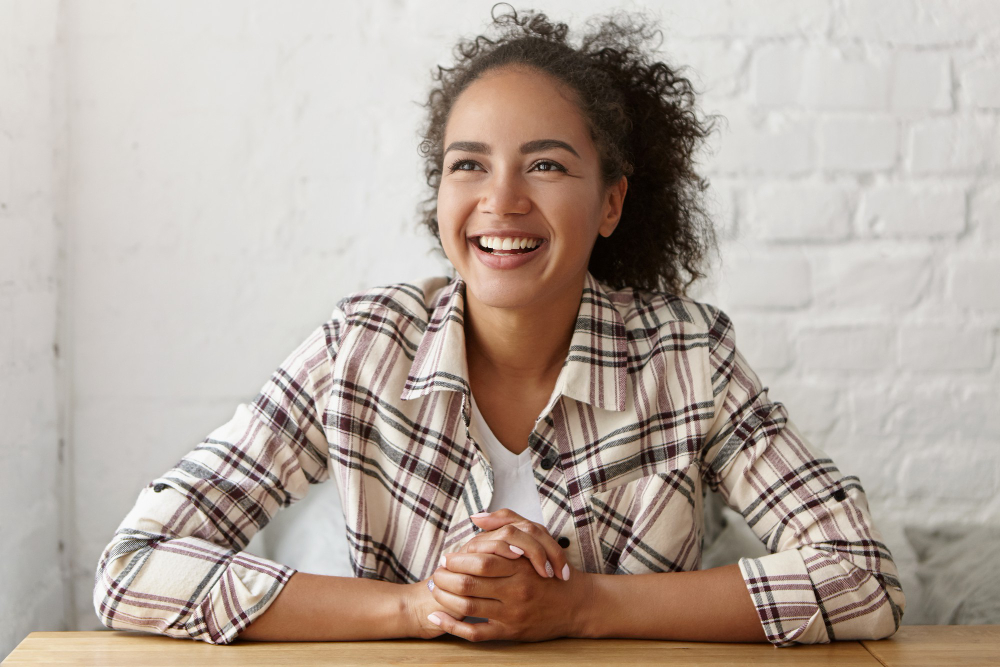 Happy smiling young woman, sitting with her hands folded.